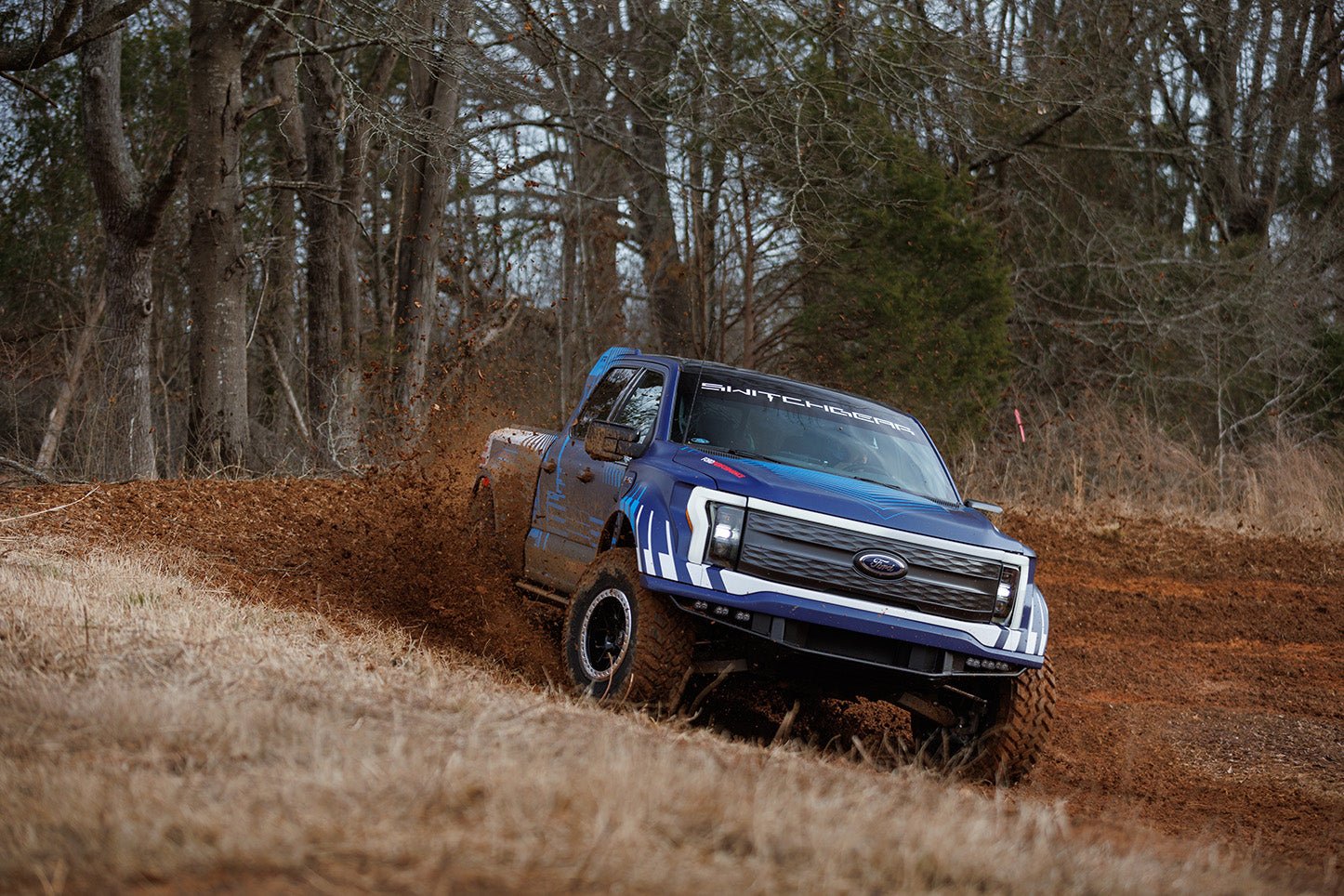 Ford Lightning Switchgear off-roading through an offroad course, showcasing electric performance and outdoor scenery with trees in the background.