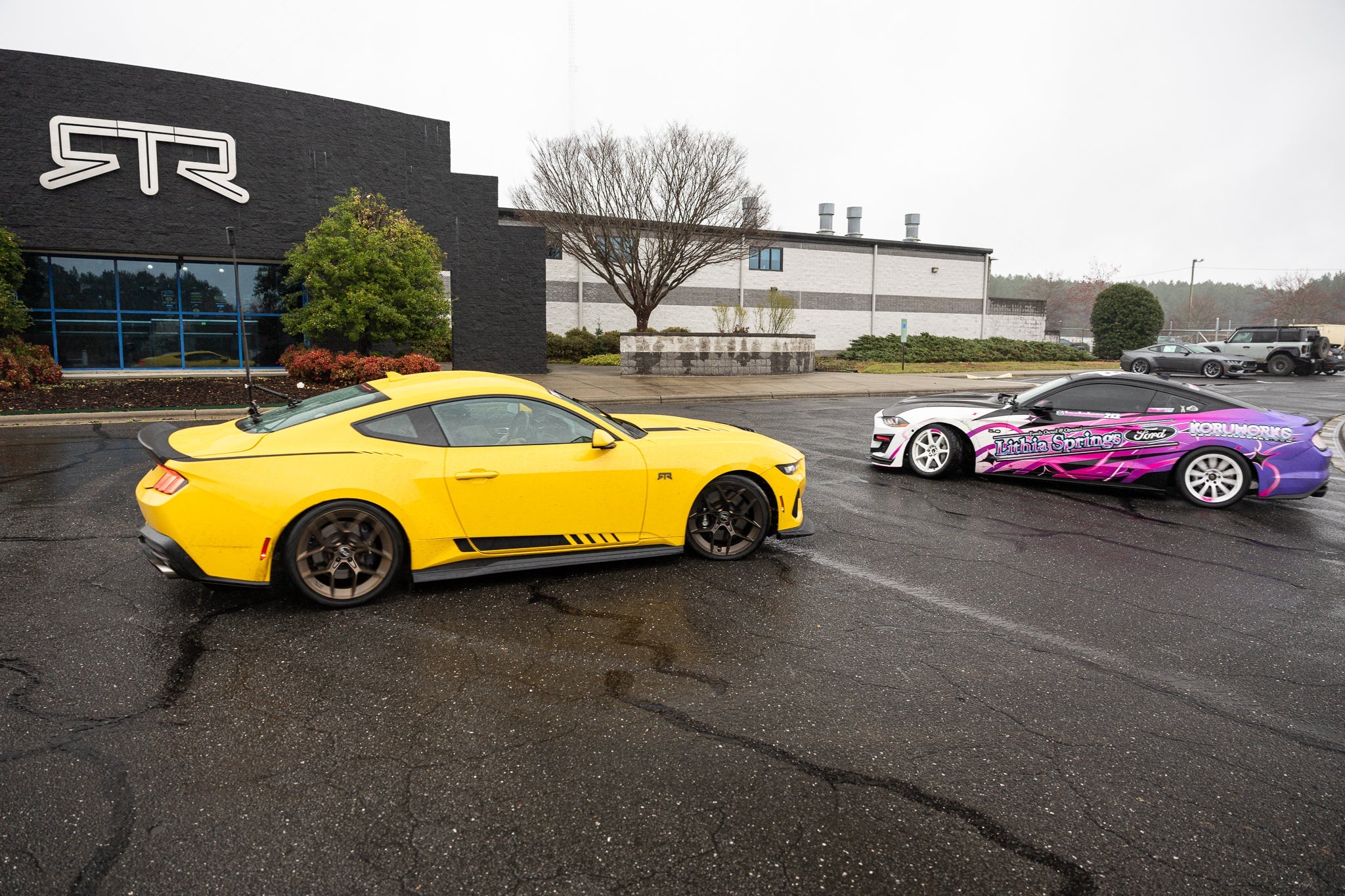 Yellow and pink Mustangs parked in front of a the RTR Lab, showcasing a vibrant automotive design with a focus on design and performance.