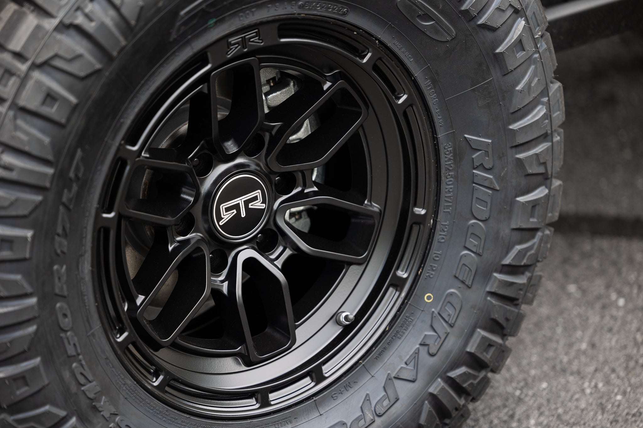 Close-up of a black RTR offroad wheel with a logo, showcasing wheels details. Automotive tire and wheel system focus.
