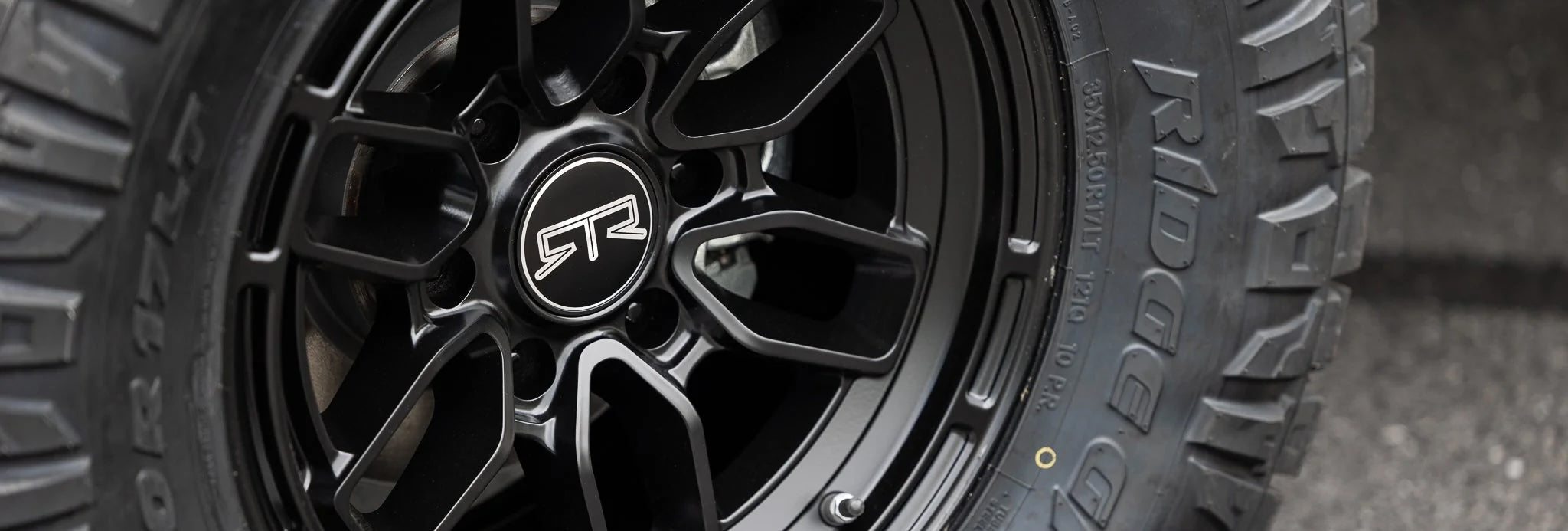 Close-up of a black RTR offroad wheel with a logo, showcasing wheels details. Automotive tire and wheel system focus.