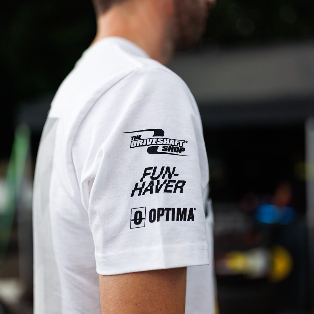 White t-shirt sleeve with black text and logos worn by a person, with a blurred background.
