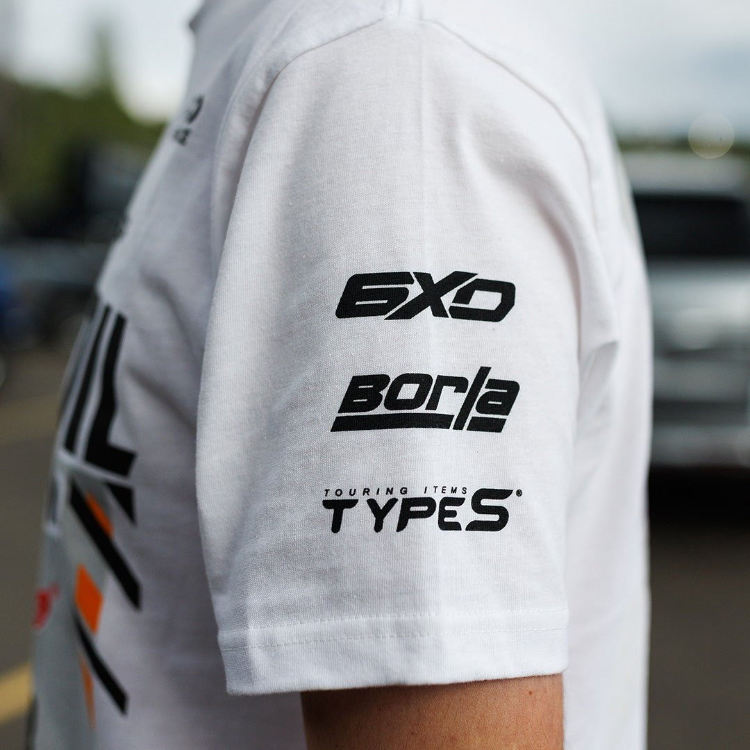 White t-shirt sleeve with black text and logos on a blurred outdoor background