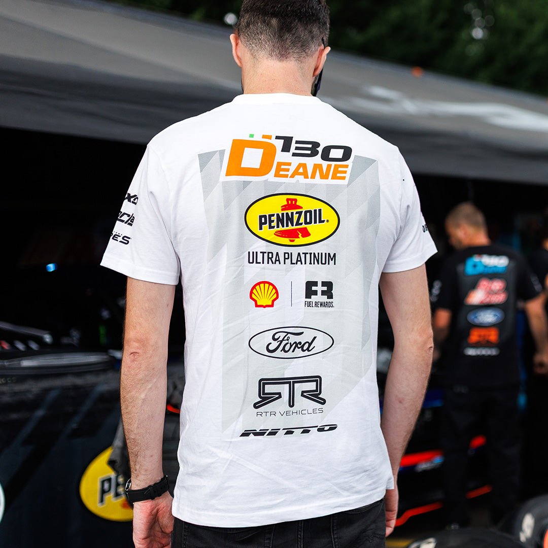 Person wearing a white t-shirt with various sponsor logos in an outdoor setting.