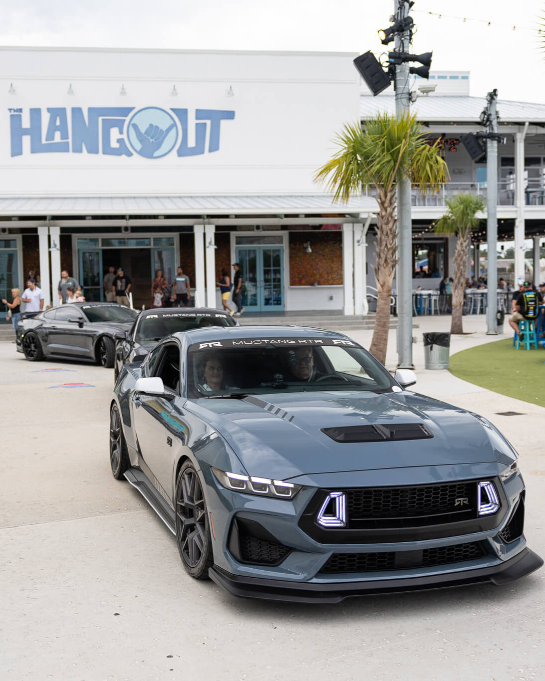 Vapor Blue Mustang RTR parked in front of a building with 'Hangout' sign