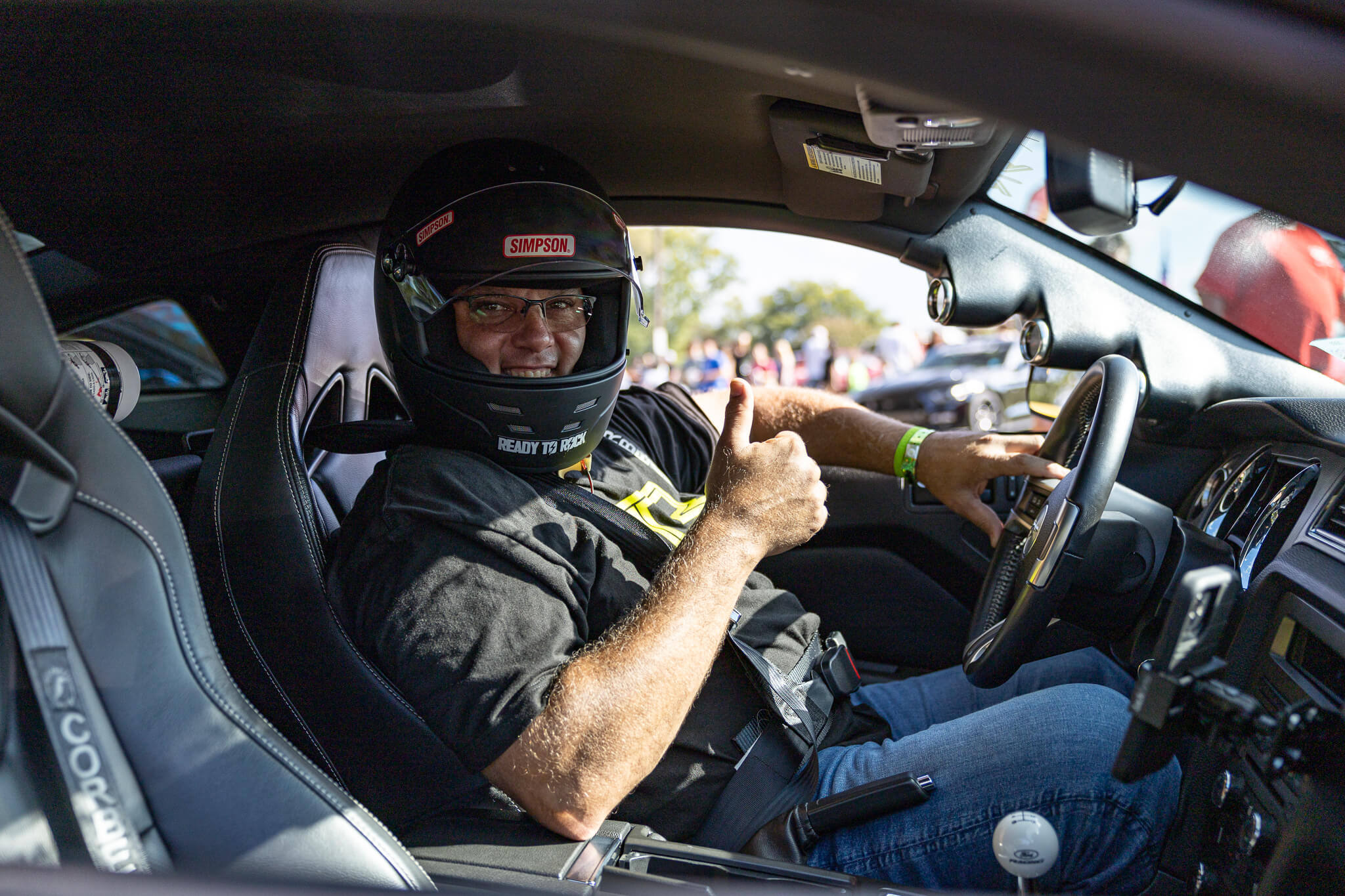 Person sitting in a Mustang wearing a helmet and giving a thumbs-up gesture.