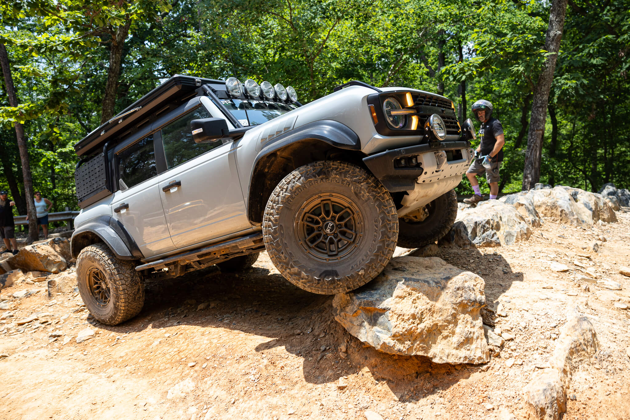 Silver off-road vehicle climbing a rocky terrain with a forest background