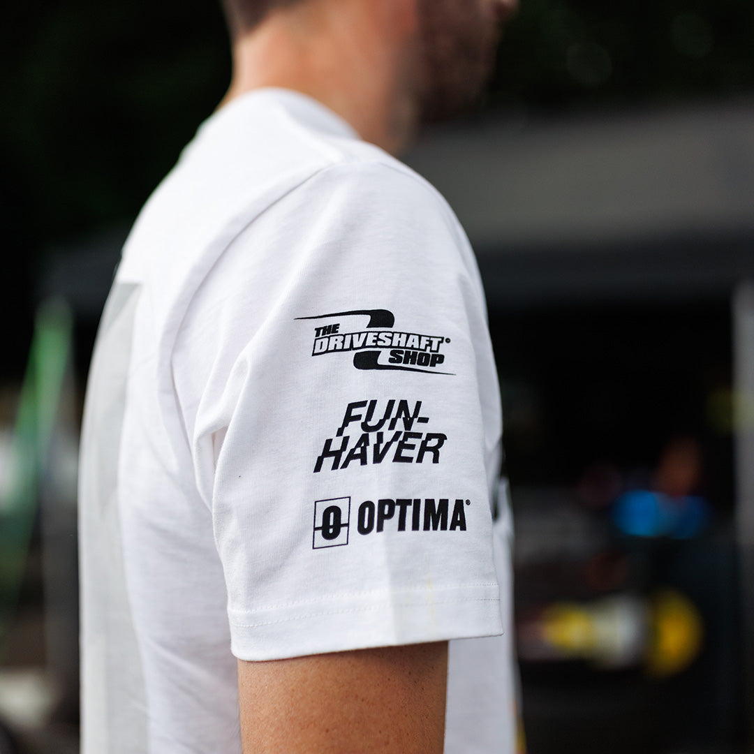 White t-shirt sleeve with black text and logos worn by a person, with a blurred background.