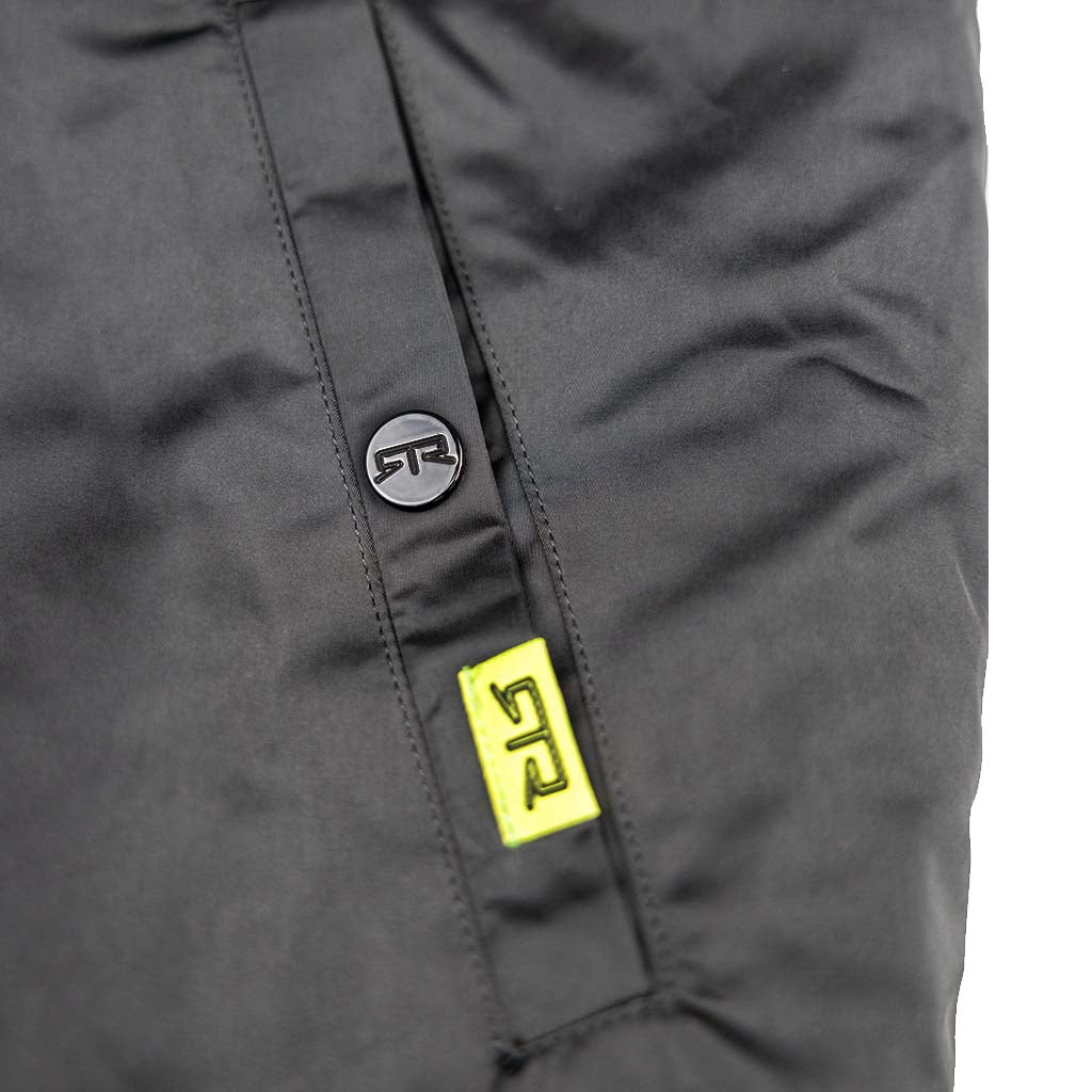 Close-up of Ford Mustang x RTR Collection Stealth Jacket showing a matte-black STR snap-button, neon-yellow STR tag, and ripstop fabric pocket detail.