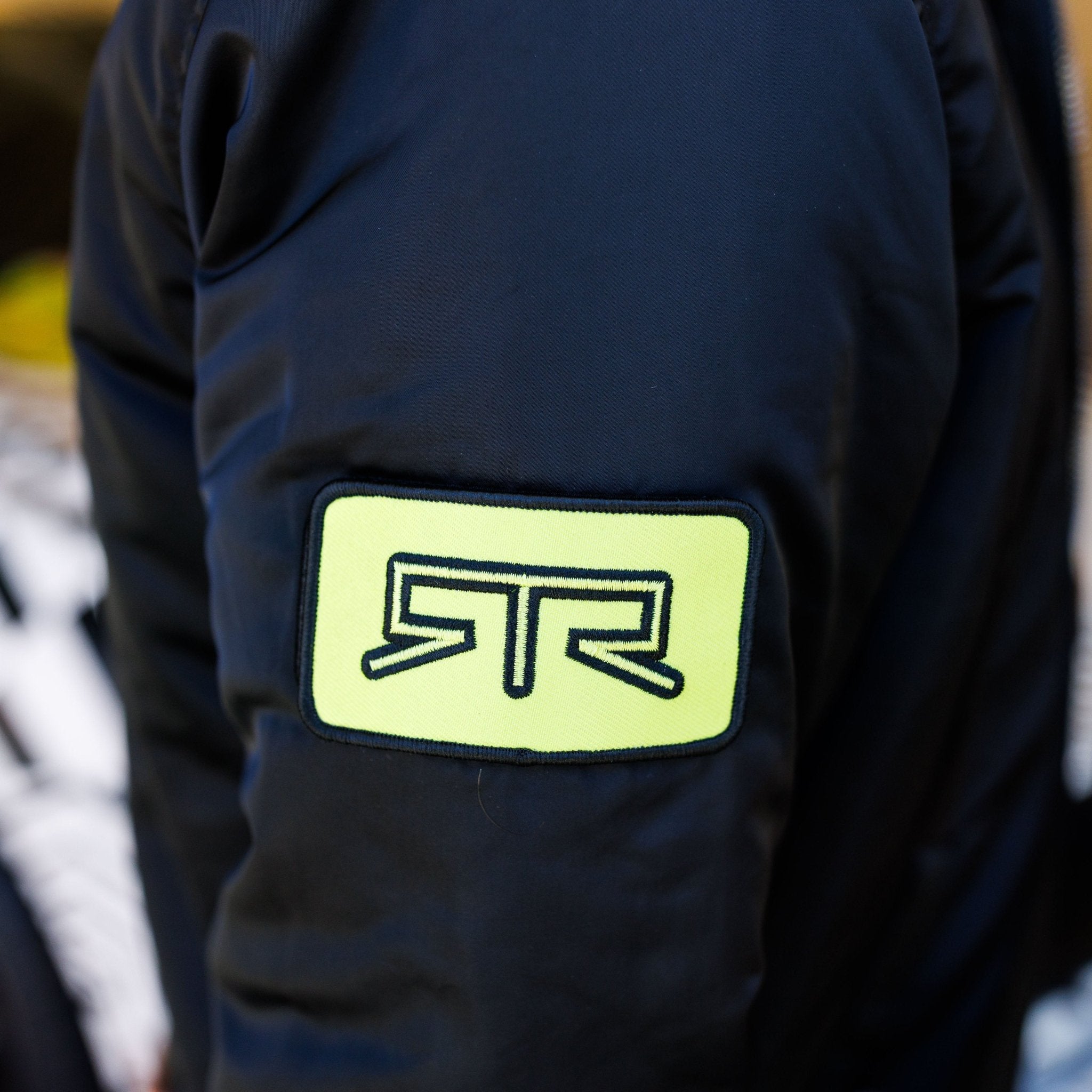 Close-up of Ford Mustang x RTR Collection Stealth Jacket sleeve with a high-visibility patch featuring the RTR logo, highlighting the jacket's performance-driven design.