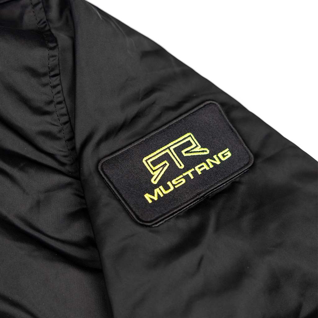 Close-up of Ford Mustang x RTR Collection Stealth Jacket sleeve with black patch, featuring bright yellow-green RTR logo above MUSTANG embroidery.