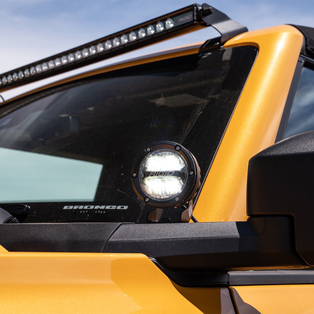 Close-up of Ford Performance by RIGID® Mirror-Mounted Off-Road Light Kit on a yellow Ford Bronco, featuring round LED light and windshield-mounted LED bar.