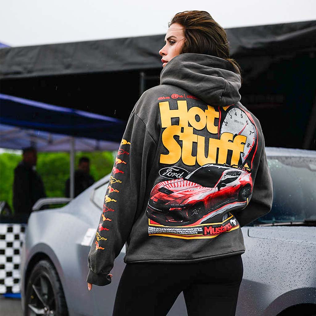 Person wearing a hoodie with 'Hot Stuff' and car graphics in front of a car.