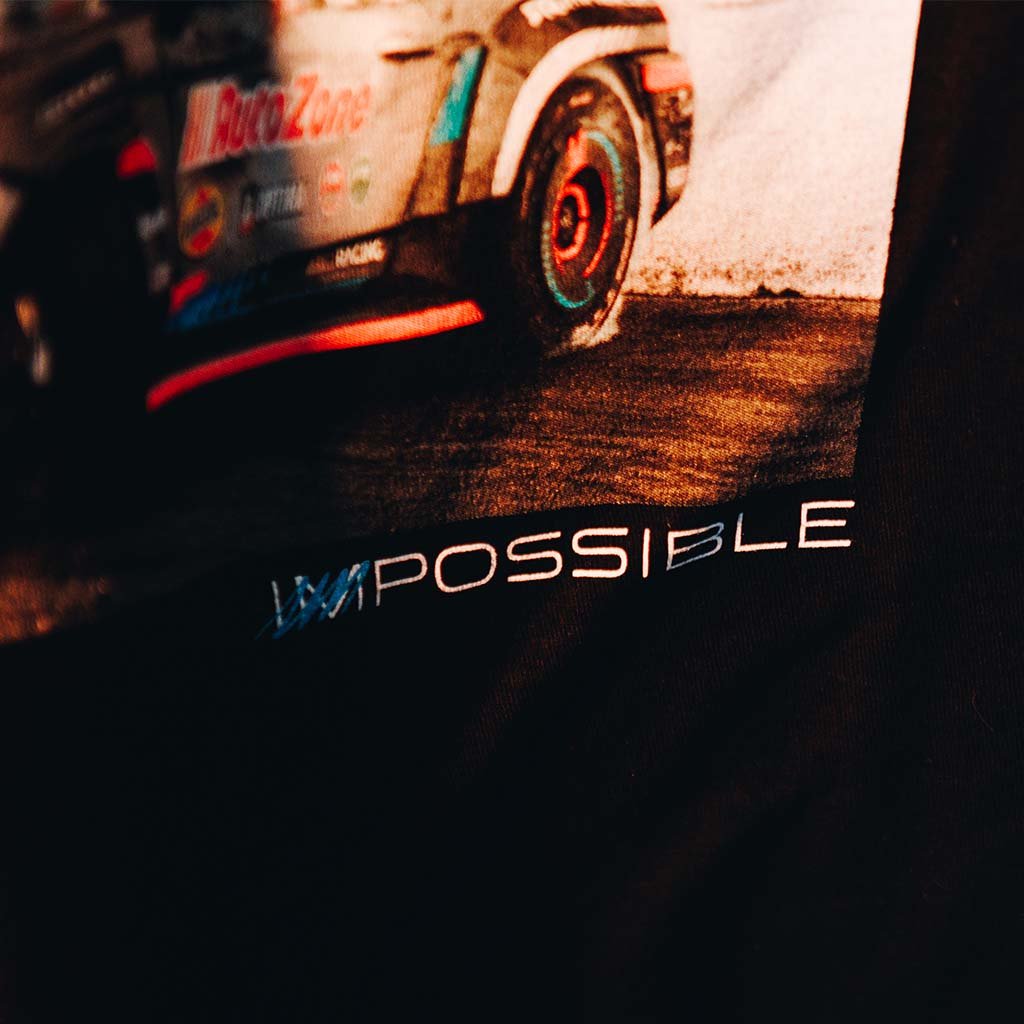 Close-up of Never Quit Tee featuring James Deane's car engulfed in smoke on track. Tee showcases 3 car panels and Never Quit motto in Deane's handwriting. Poster includes Deane's signature and message.