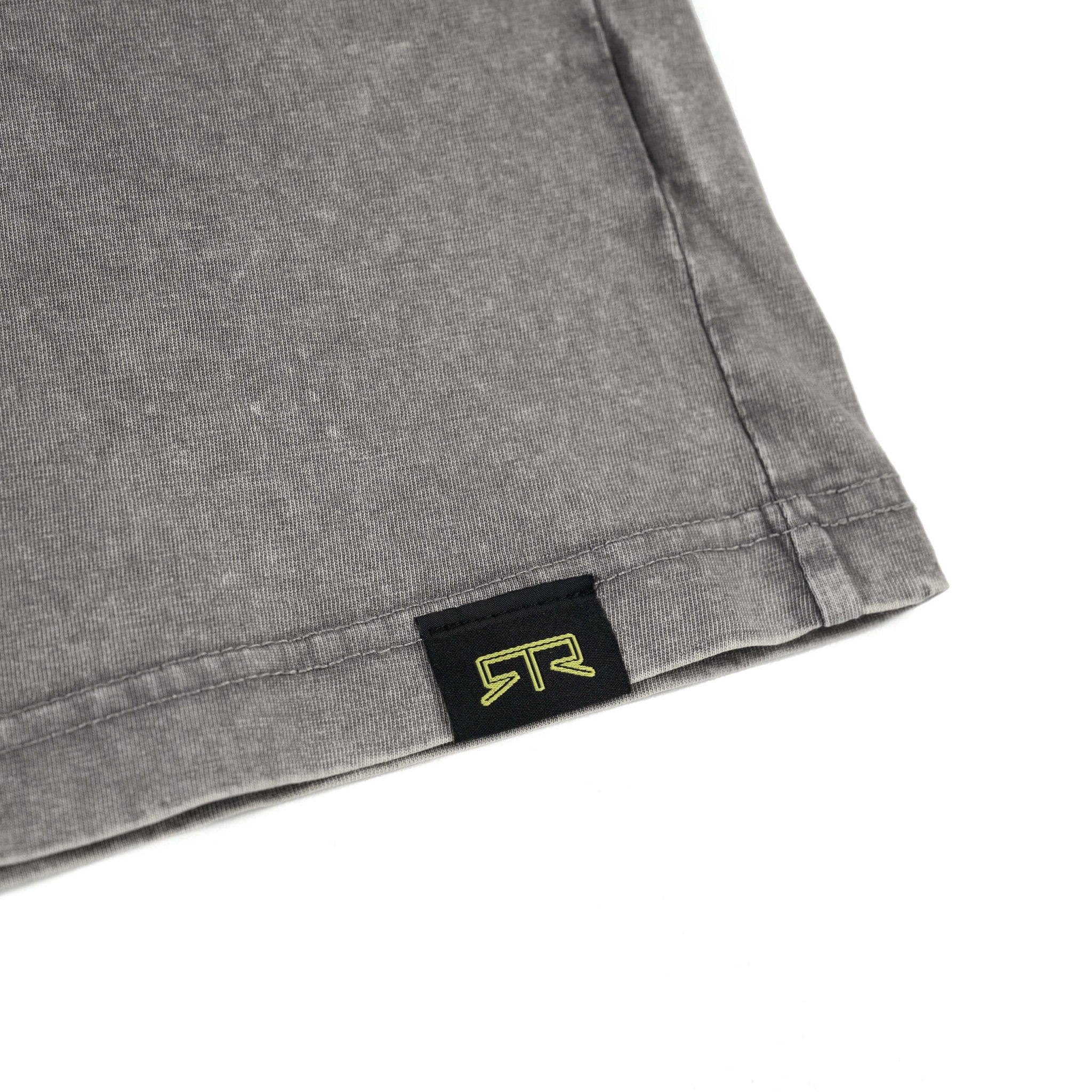 Close-up of RTR Distressed T-Shirt label and logo on grey fabric, highlighting the woven hem tag and signature style details.