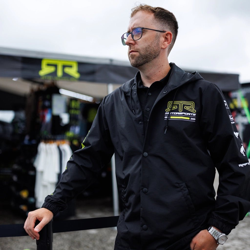 RTR Team member wearing the Black and Hyperlime RTR Motorsports Windbreaker Waterproof Jacket in front of the RTR Vehicles rig at Formula Drift.