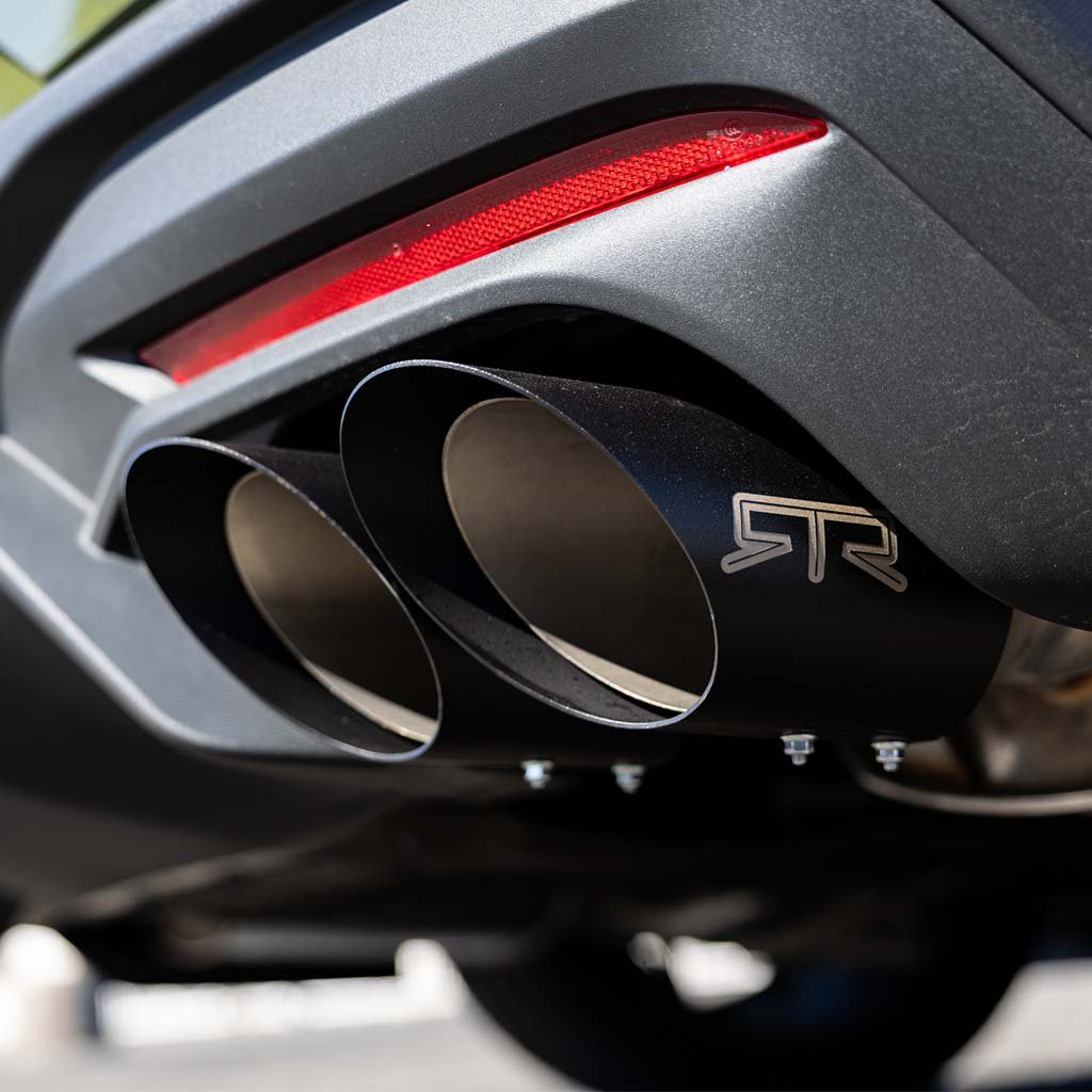 Close-up of RTR Quad Tip Cover Kit for 2015+ Mustang, showing black, dual exhaust tips with stamped logo and red reflector above.