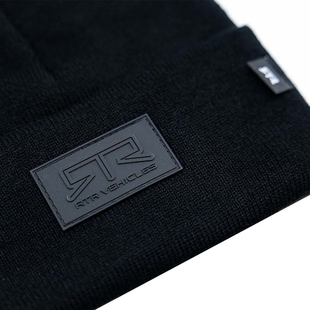 A black beanie with a rubberized RTR logo stitched on it, embodying the RTR Blackout Beanie's sleek design and understated style.
