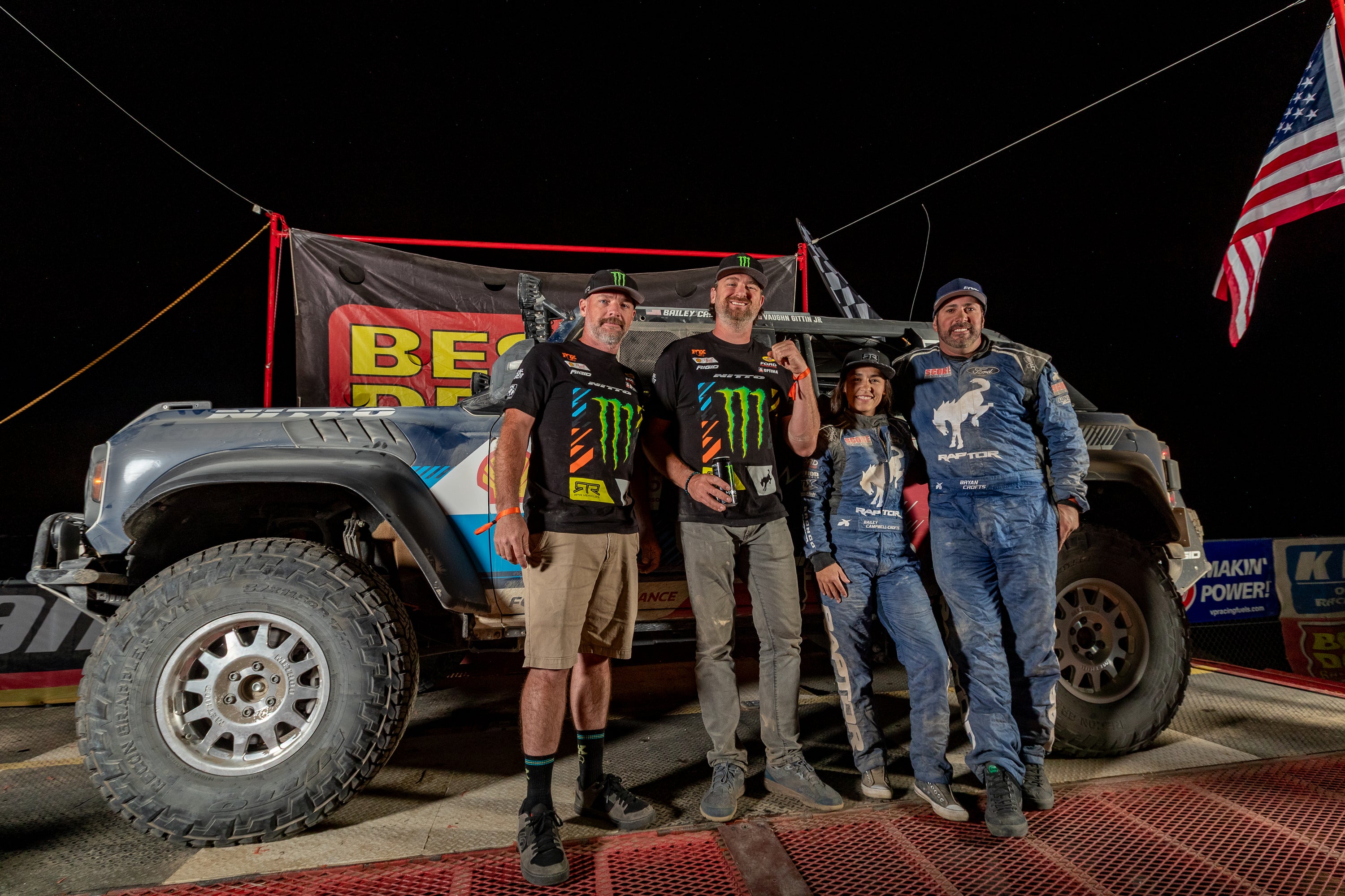 Members of the RTR Vehices Off-Road team standing in front of a truck with sponsor logos at night.
