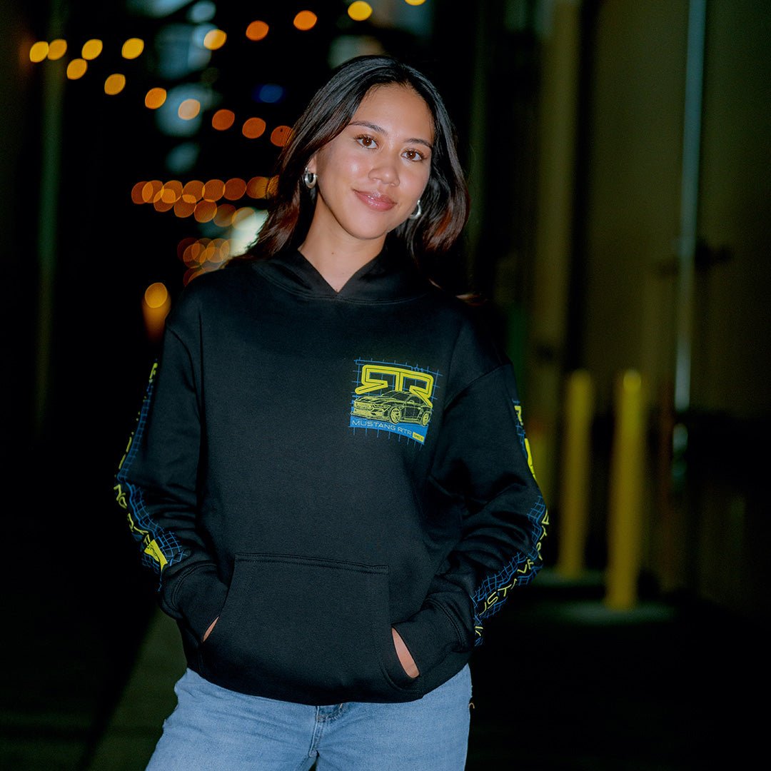 Woman wearing a black Spec 5 Blueprint hoodie with RTR logo, standing against a blurred background with lights.