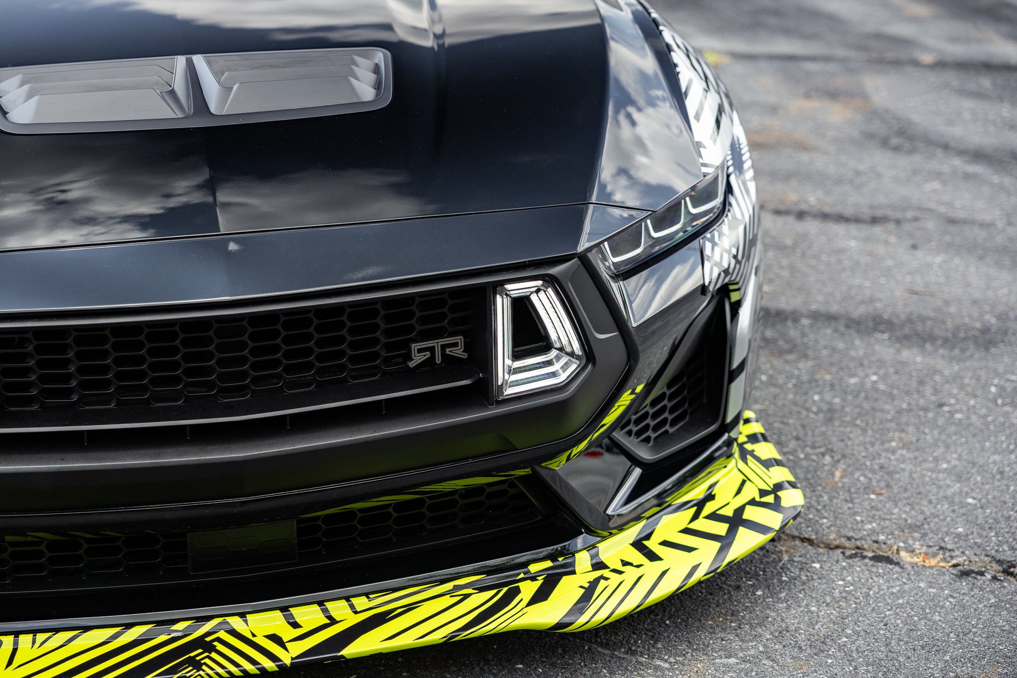 Close-up of a black 2026 Mustang RTR Spec 5 with a hyperlime and black camouflaged front components on a road.