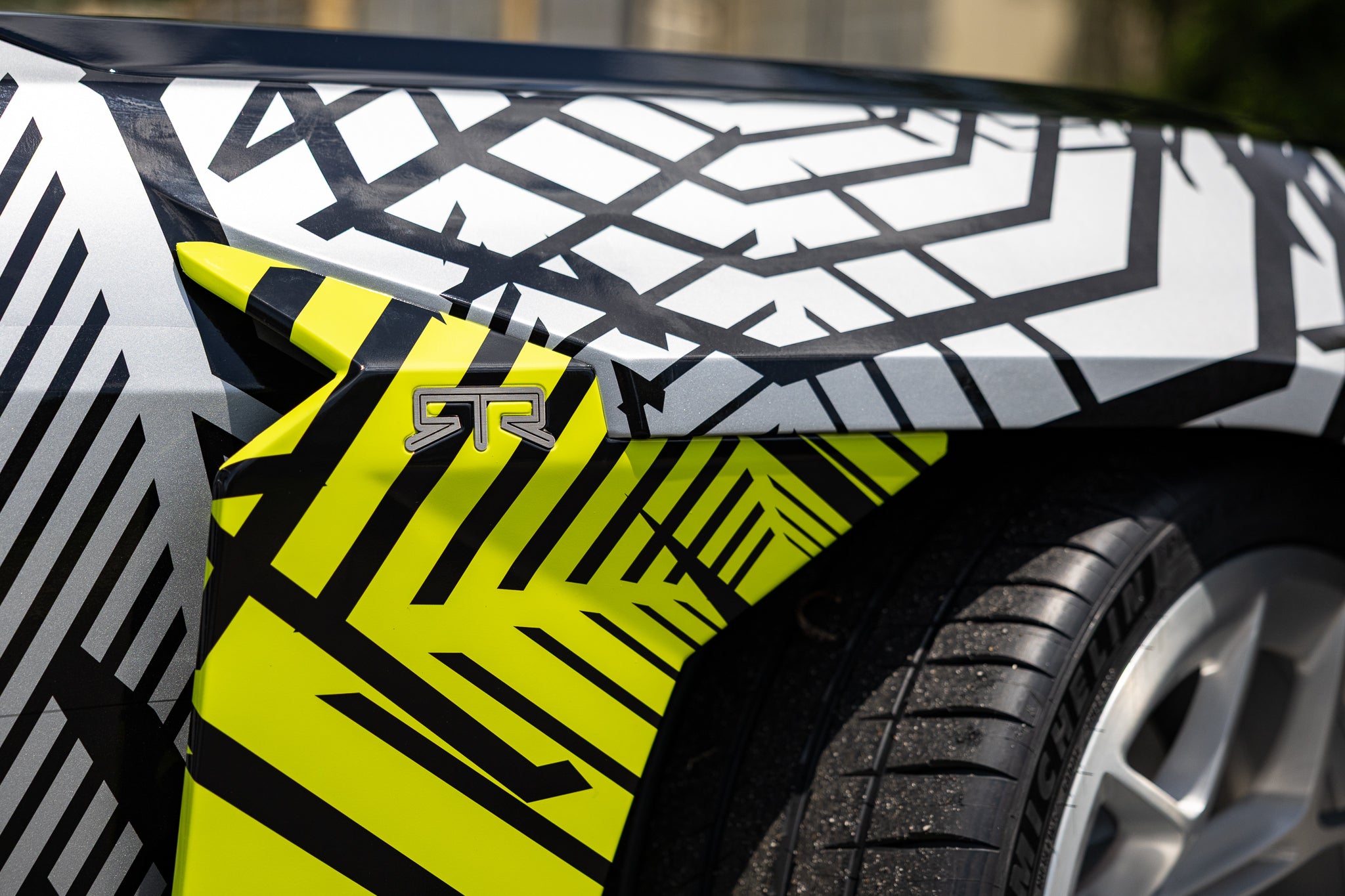 Deatil image of the fender of a black 2026 Mustang RTR Spec 5 with a hyperlime and black camouflaged front components.