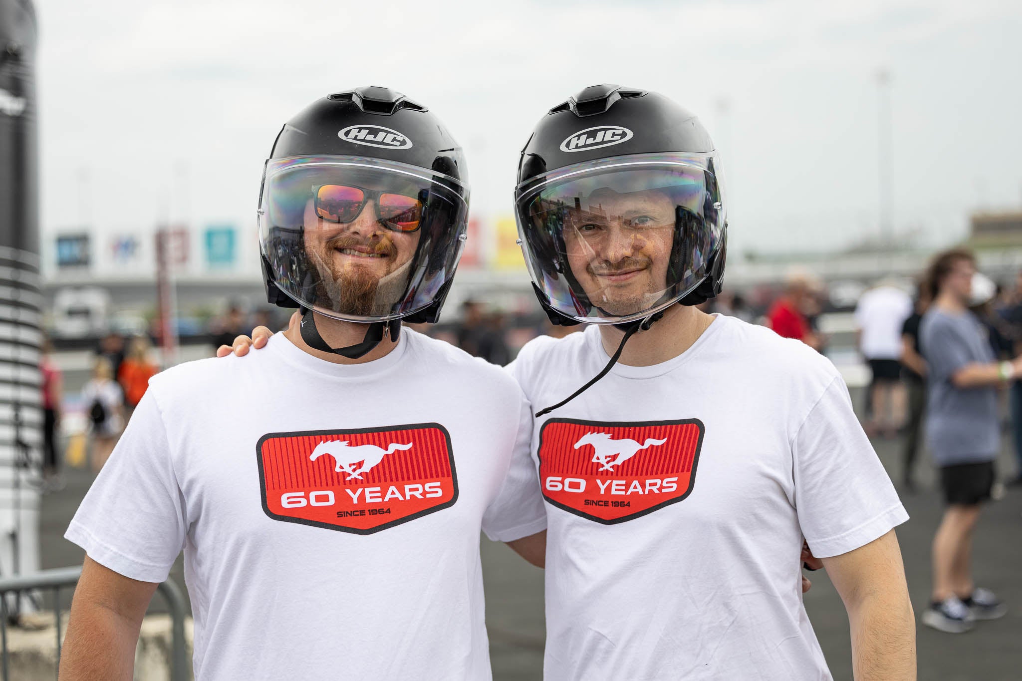 Two men in white Mustang 60th tees and helmets pose for a picture