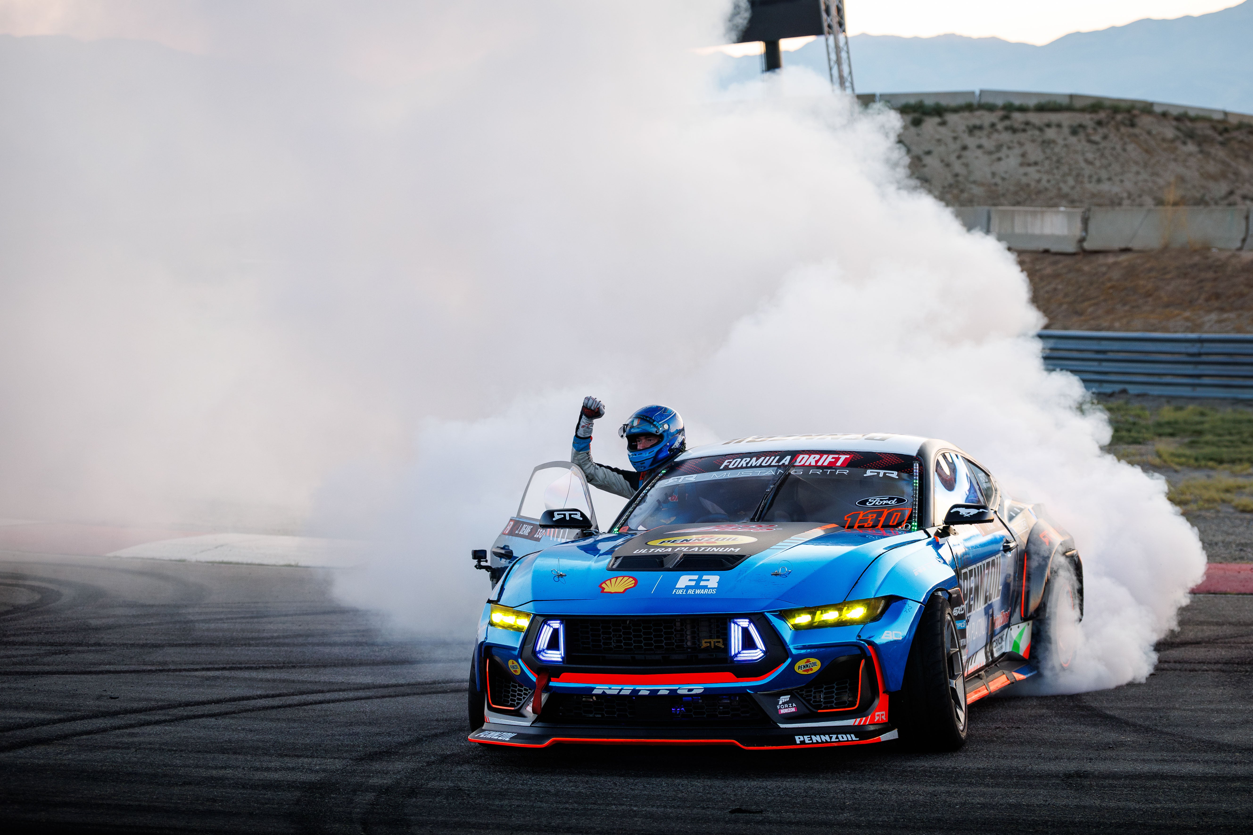 Blue race car performing a drift with smoke on a track