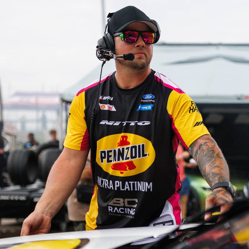 RTR Vehicles crew member wearing the Ben Hobson 2026 RTR Drift Team Sublimated Shirt with race communications headset in the pit lane at a Formula Drift event.