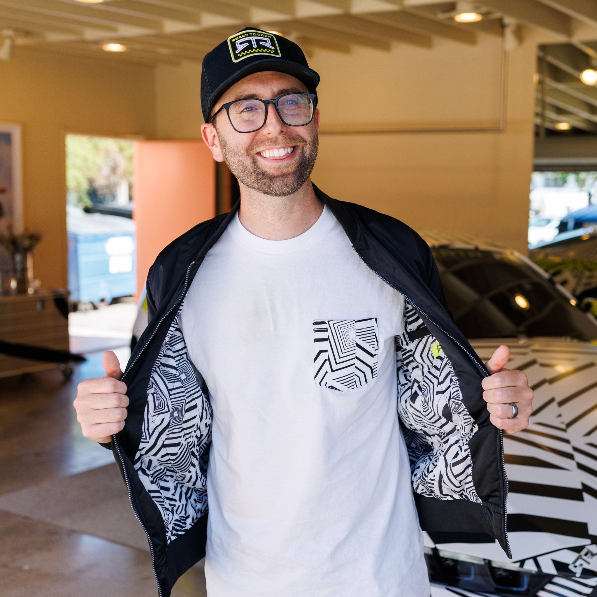 Man showcasing Ford Mustang x RTR Collection Stealth Jacket, revealing black-and-white geometric lining, matching car pattern in background, emblematic of modern performance and style.