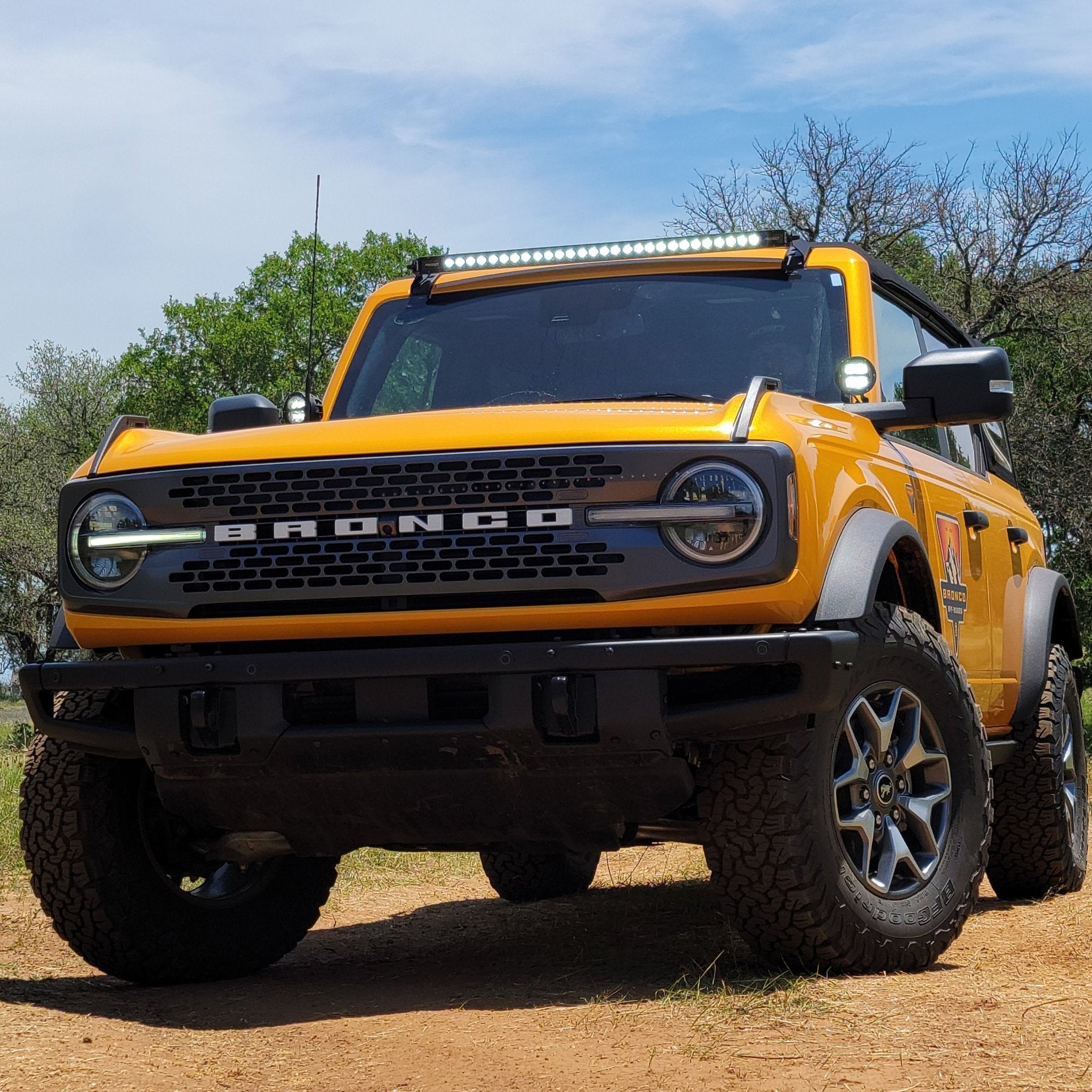 Yellow Ford Bronco SUV on a dirt road with trees in the background