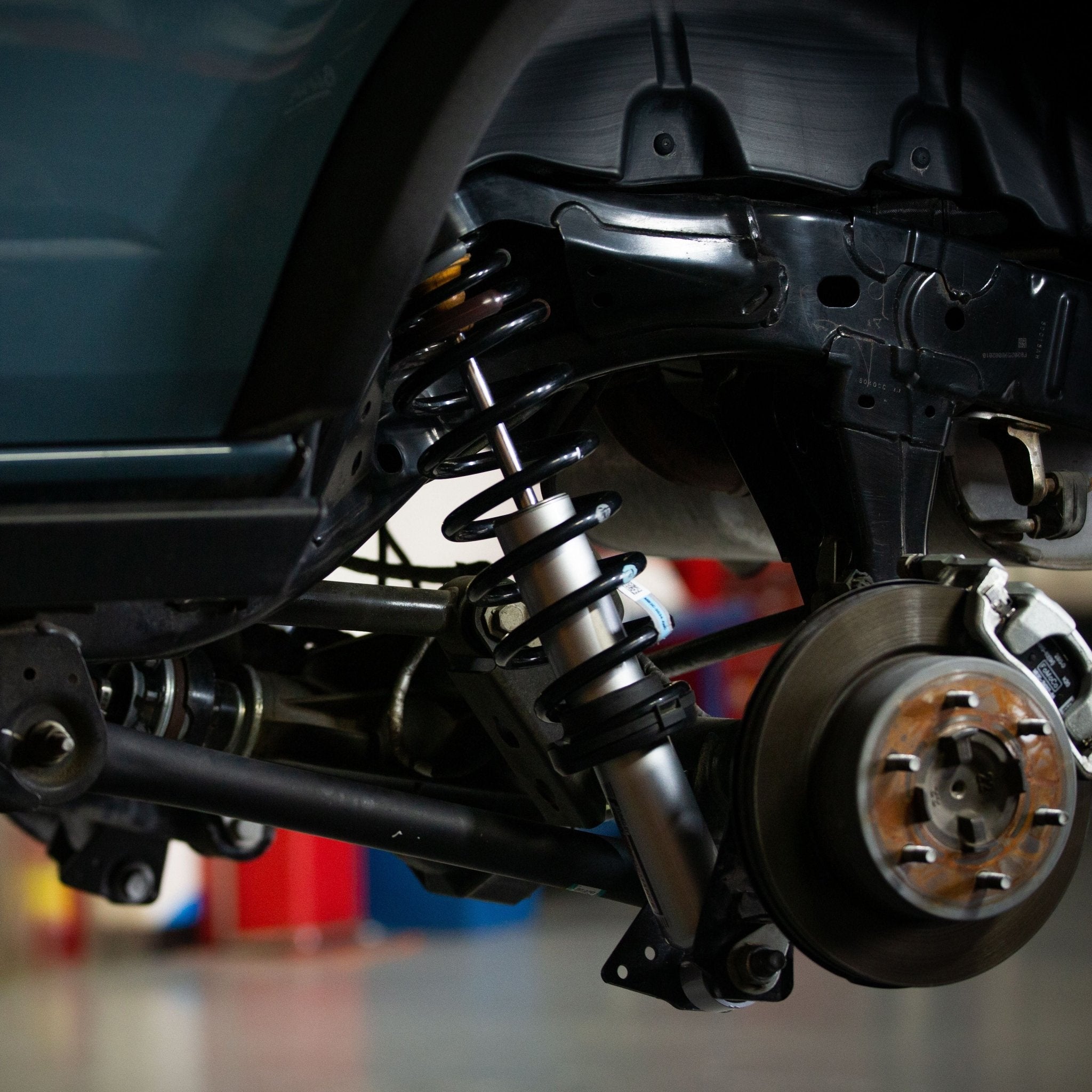 Ford Performance Off-Road Suspension 2 Lift Kit (21+ Bronco) featuring a coil-over shock absorber, control arm, and brake assembly, displayed on a lifted vehicle in a garage.