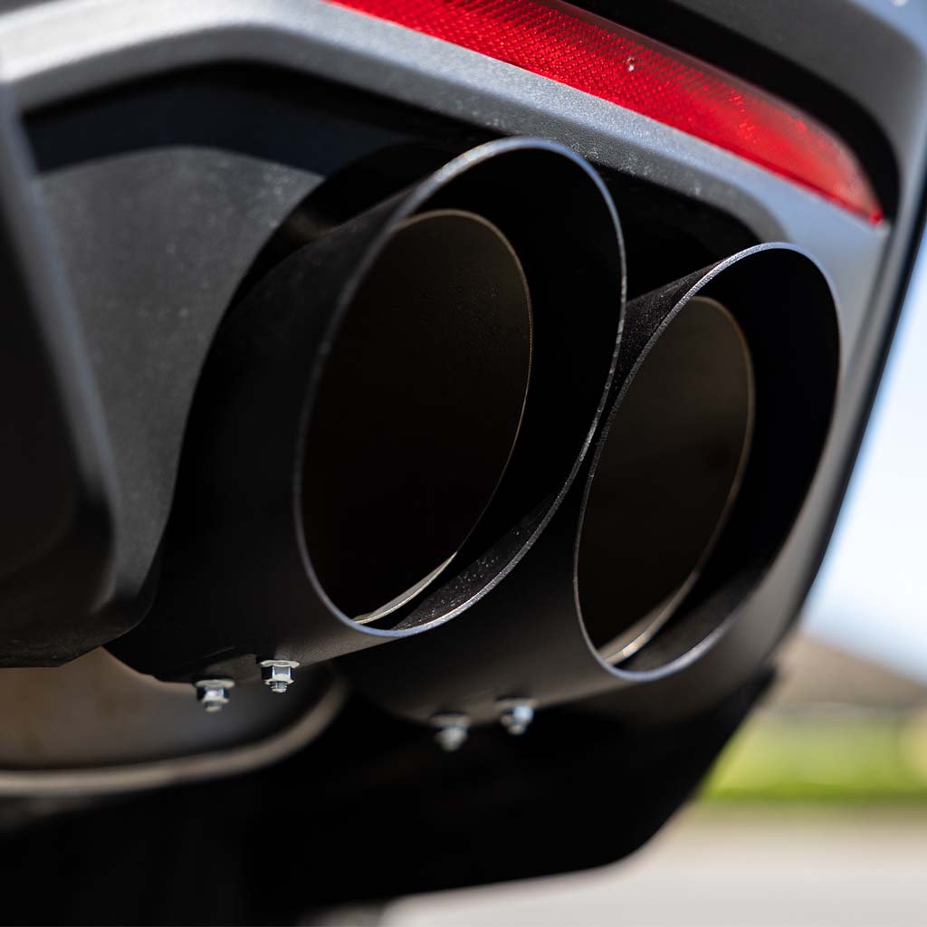 Close-up of an RTR Quad Tip Cover Kit on a 2015+ Mustang, showcasing dual tailpipes with smooth, angled covers, and a hint of rear light trim.