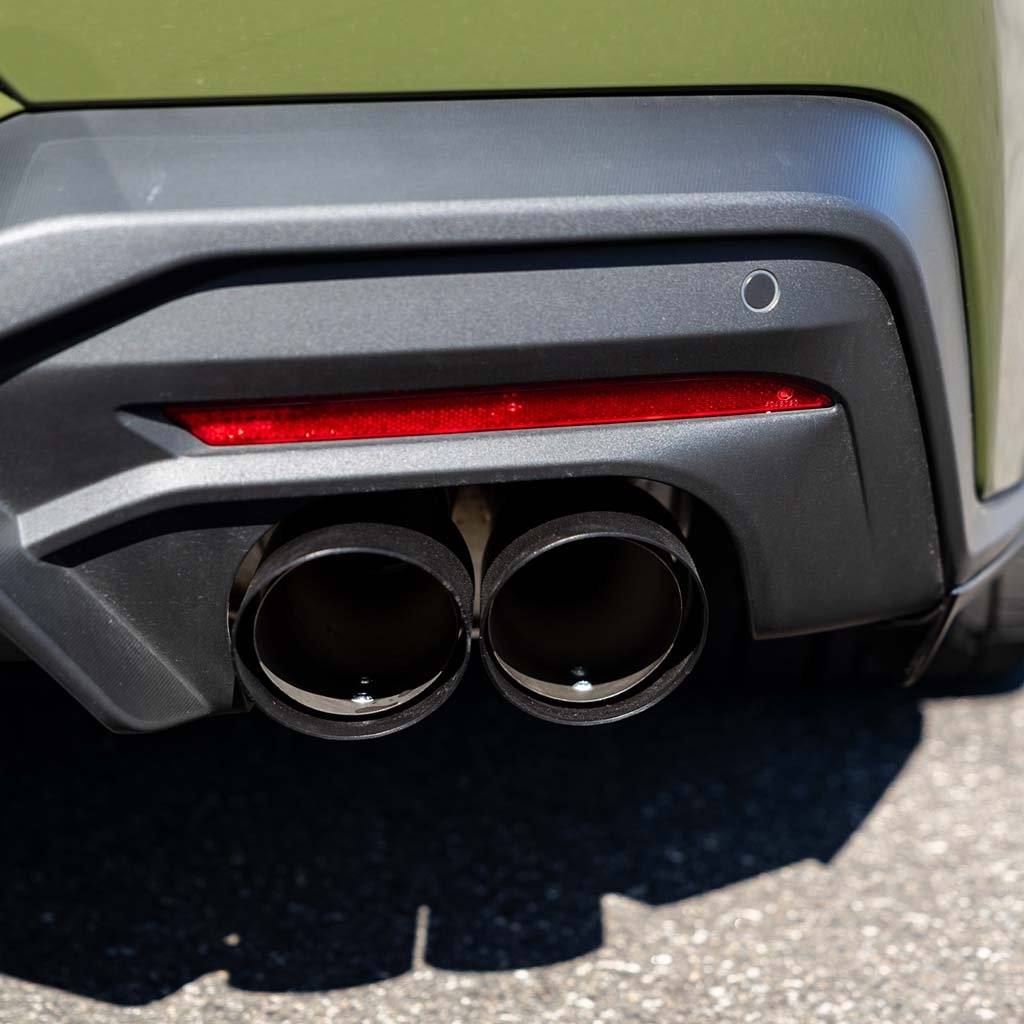 RTR Quad Tip Cover Kit (15+ Mustang) installed on a car, highlighting dual tailpipes with black diffuser, red reflector, and parking sensor for an aggressive rear look.