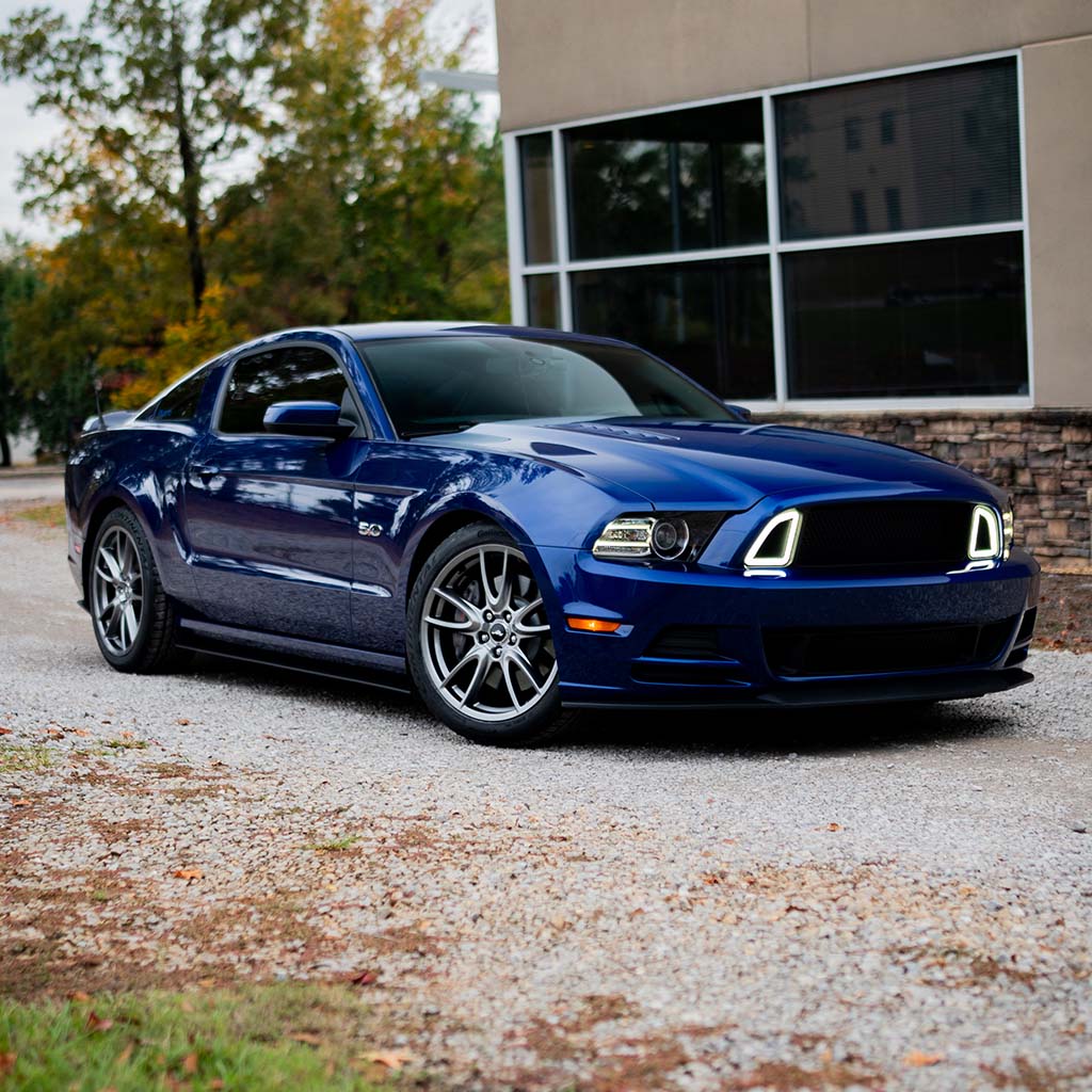 Deep-blue Ford Mustang with RTR Upper Grille featuring Signature LED Accent Lighting, showcasing its aggressive design and enhanced airflow on a gravel driveway.