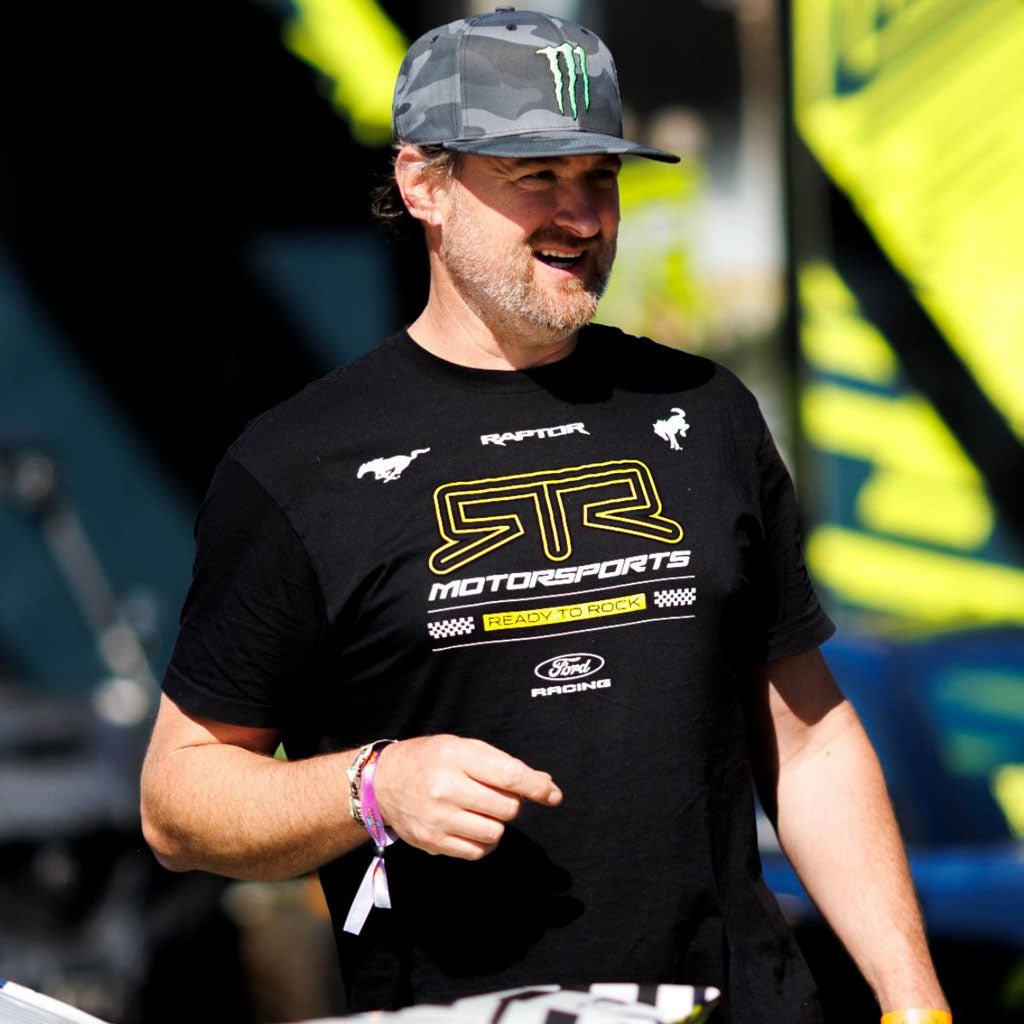 Vaughn Gittin Jr. wearing the Black, Short Sleeved 2026 RTR Motorsports Essential Heritage T-Shirt while wearing a camouflage Monster Energy hat.