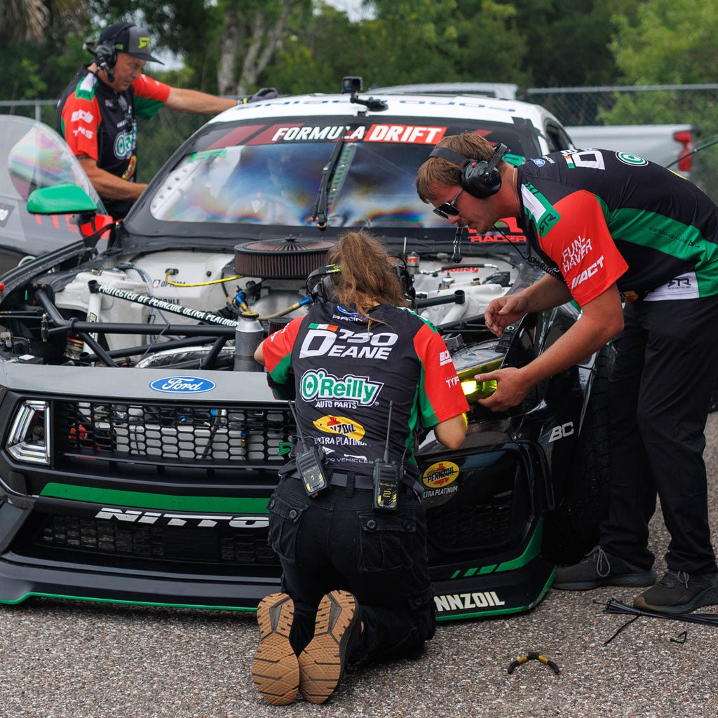 RTR Vehicles crew members wearing the James Deane 2026 RTR Drift Team Sublimated Shirts while wrenching on  James Deane's Ford Mustang RTR at a Formula Drift event.