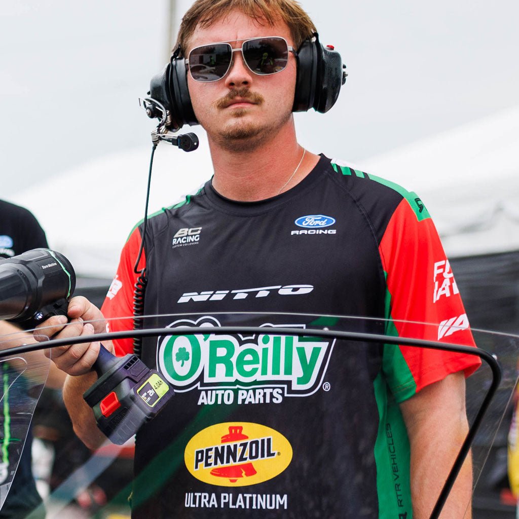 RTR Vehicles crew member wearing the James Deane 2026 RTR Drift Team Sublimated Shirt pit-side at a Formula Drift event, with race communications headset and equipment.