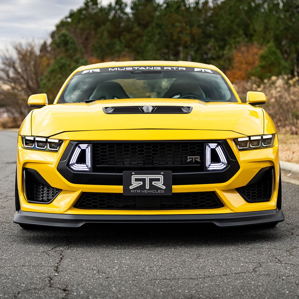 Front view of a yellow Mustang with RTR Front License Plate Bracket, showcasing RTR Upper Grille and LED Air Intakes compatibility. Crafted from black powder-coated aluminum with RTR logo.