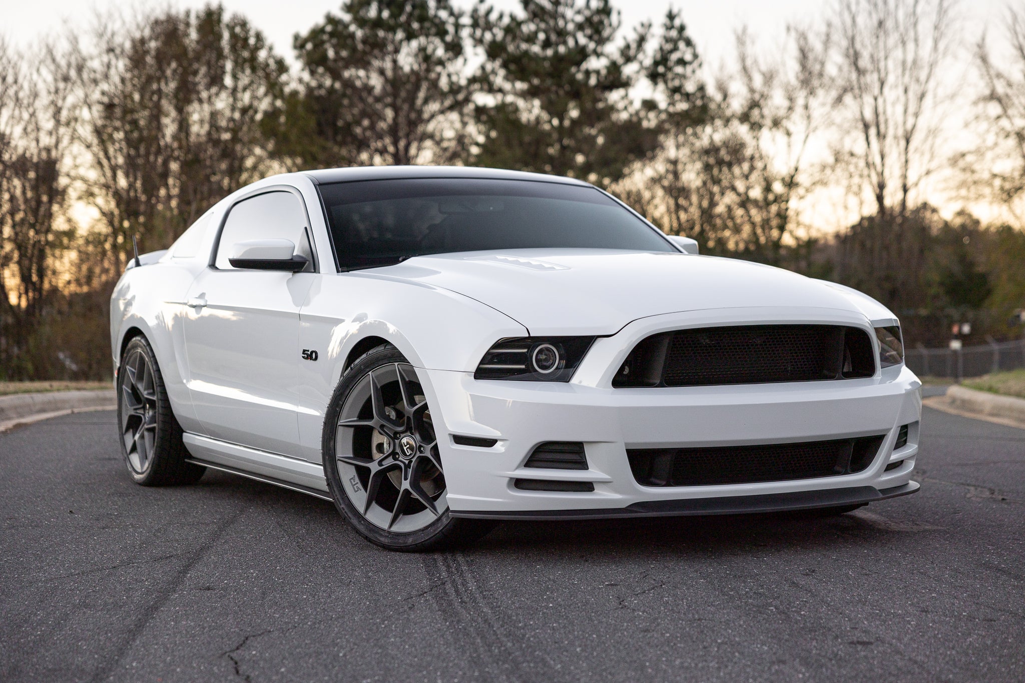 A white Mustang GT with RTR Upper and Lower Grilles parked on a road. Modern aggressive styling inspired by Mustang RTR, designed for 2013-2014 models. Enhances airflow and engine cooling.